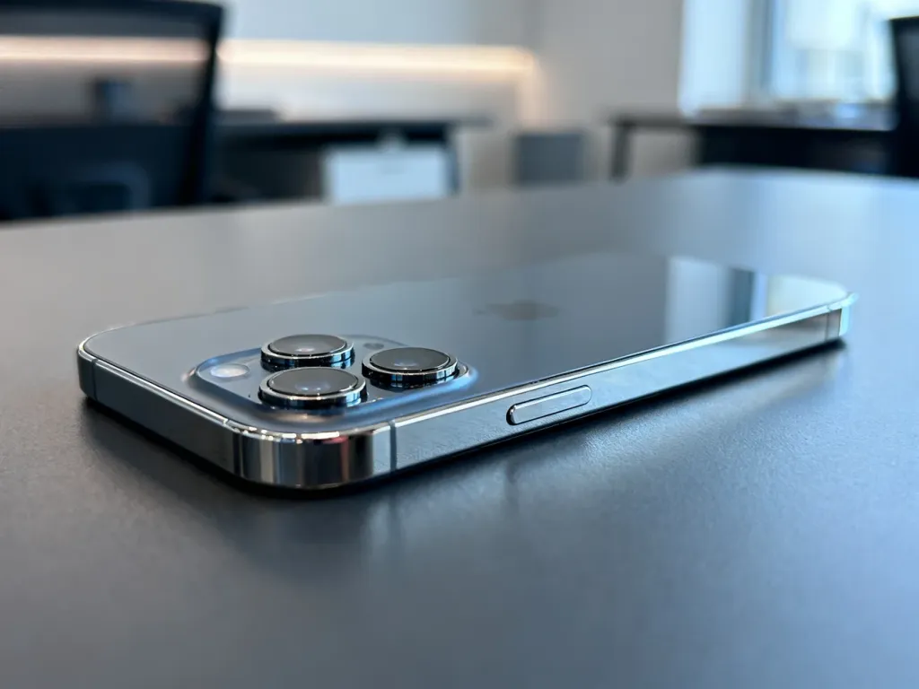 Zbliżenie na elegancki iPhone 12 Pro z potrójnym aparatem i polerowaną ramką, leżący na minimalistycznym biurku.